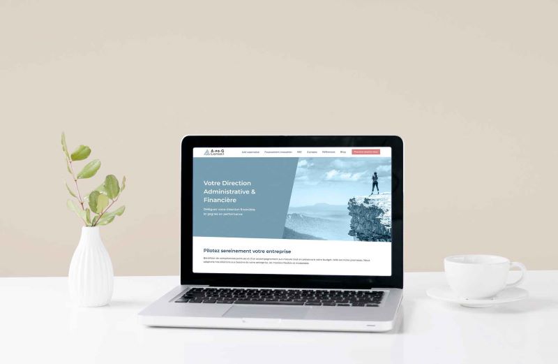 Présentation du site internet sur un écran d’ordinateur portable posé sur un bureau blanc avec une tasse blanche et un vase contenant une branche
