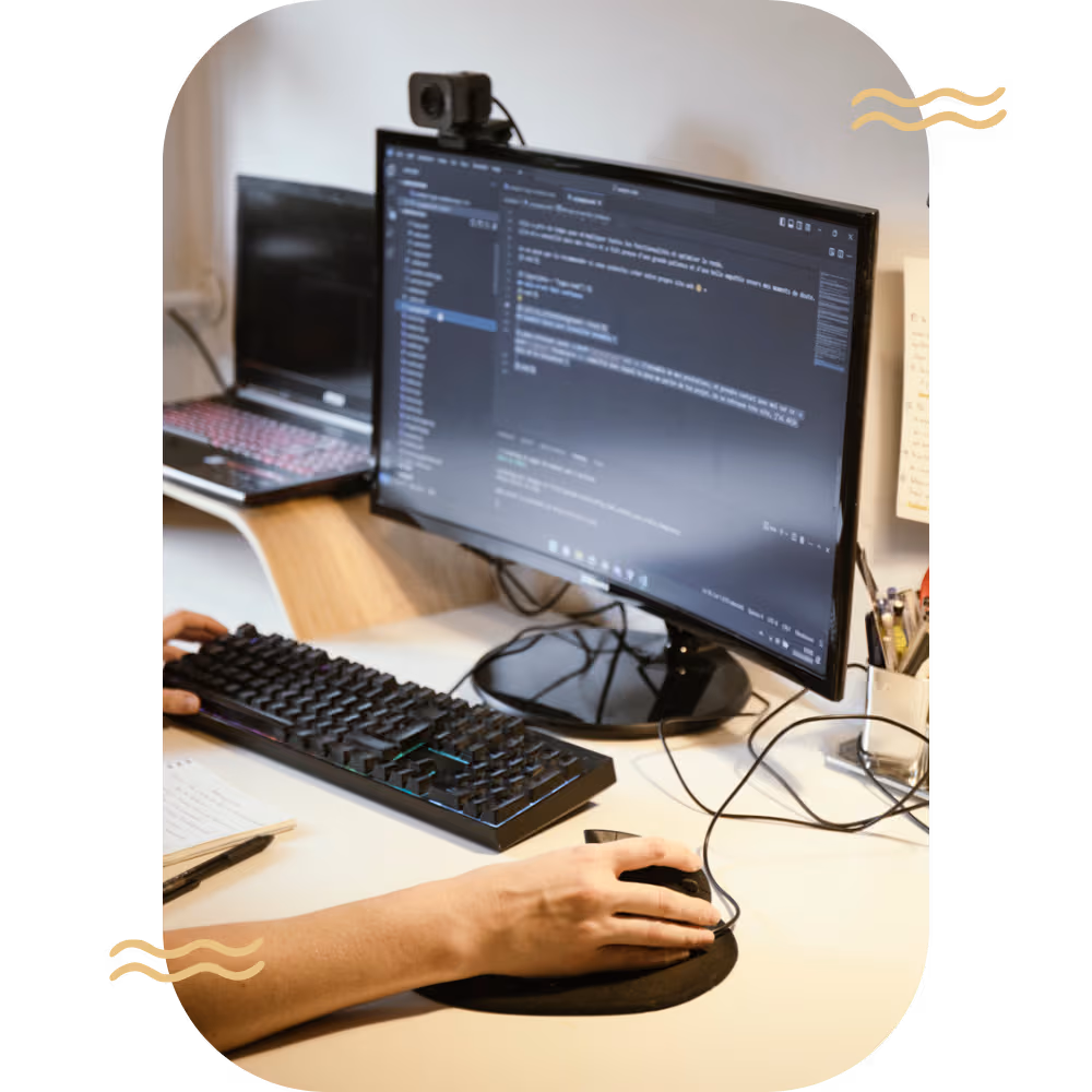 Bureau avec clavier, main sur la souris et écrans d’ordinateurs avec fenetre de code